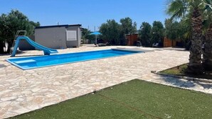 A swimming pool with a slide, surrounded by a stone patio and a grassy area.