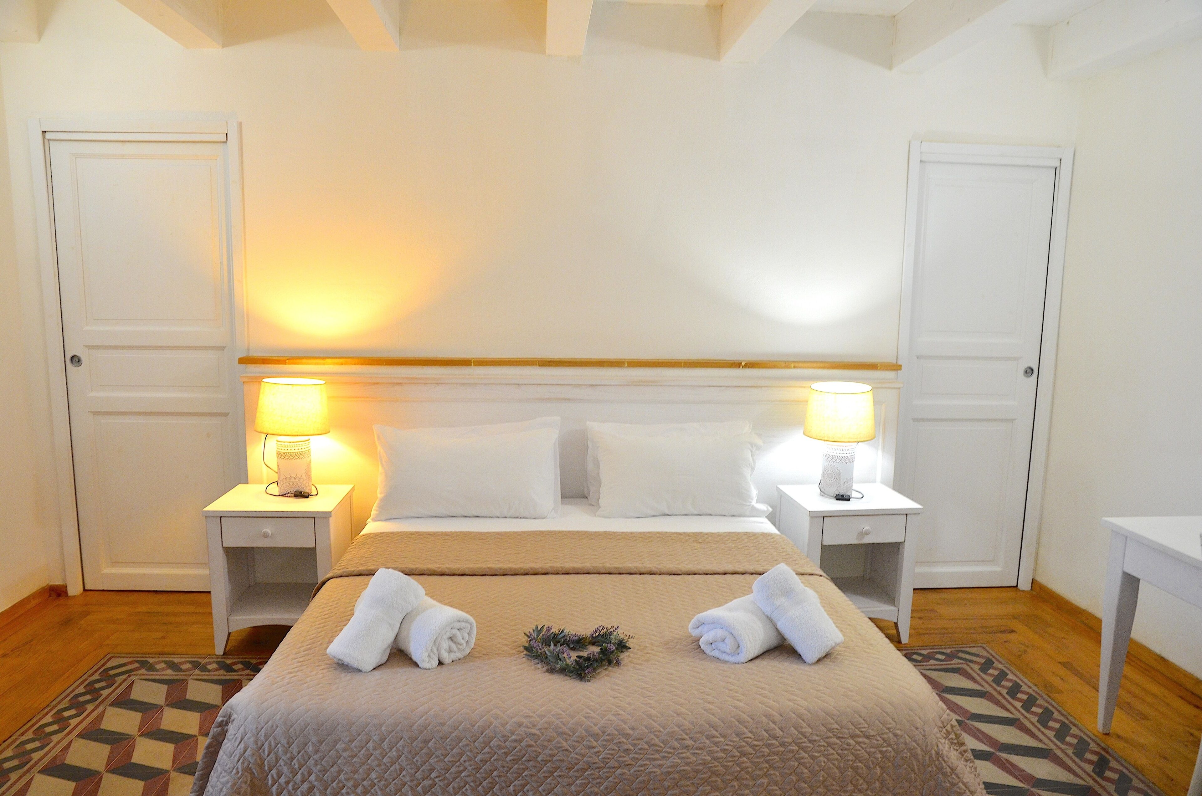 A neatly arranged hotel room with a bed, two bedside tables with lamps, a patterned rug, and a small decorative wreath on the bed.