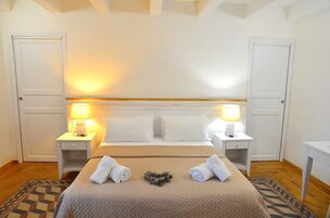 Habitación de hotel ordenada con una cama, dos mesitas de noche con lámparas, una alfombra estampada y una pequeña corona decorativa sobre la cama.