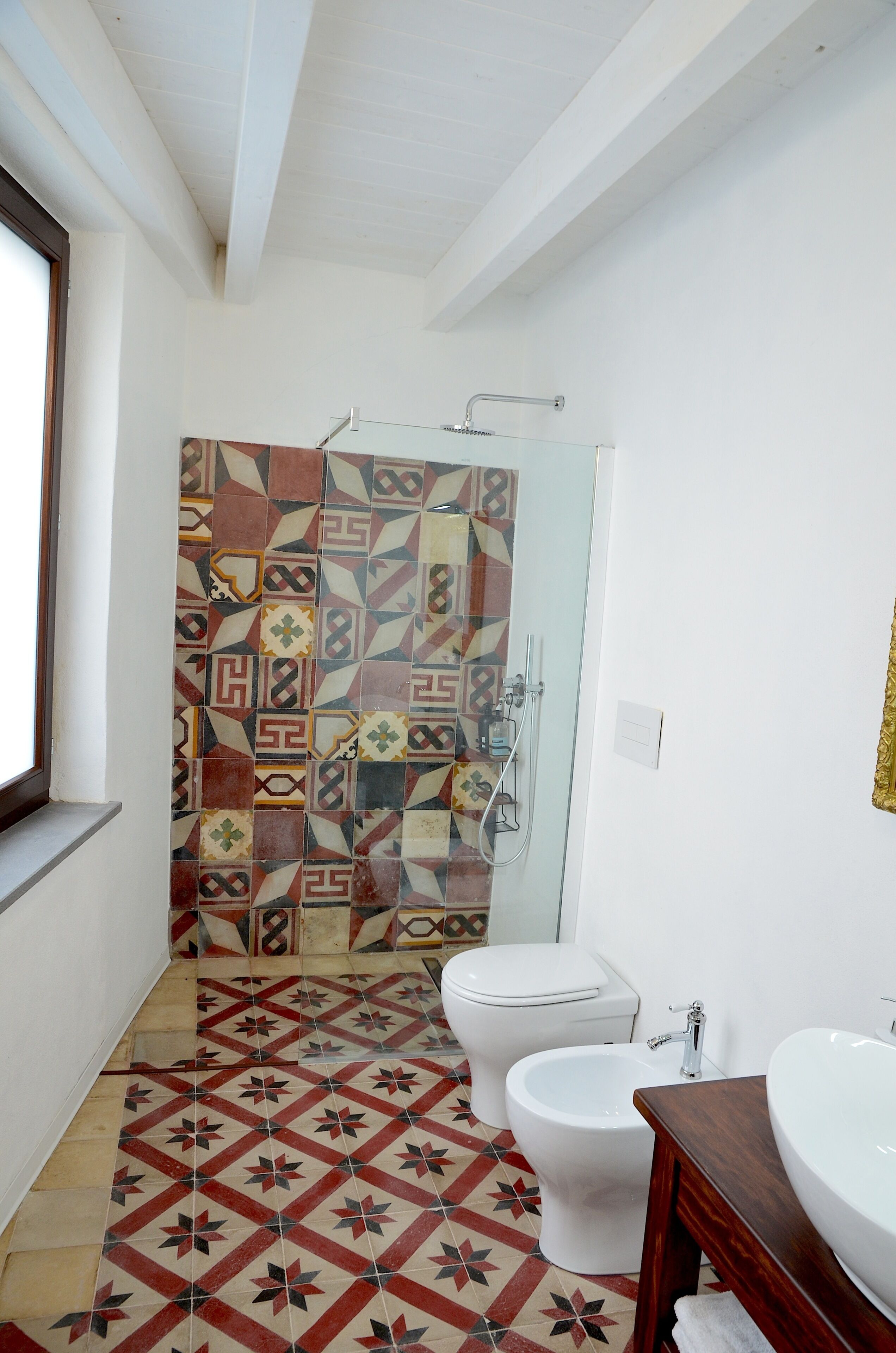 A bathroom with patterned tiles, a toilet, a bidet, and a sink.