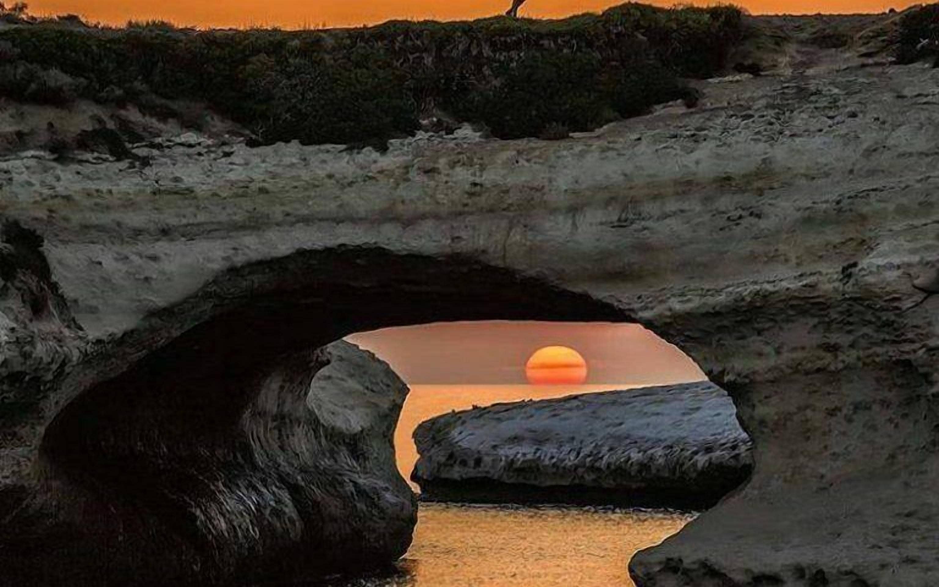 Un atardecer a través de un arco natural de roca sobre una masa de agua.