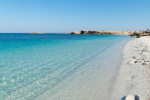 A beach with clear turquoise water and white sand, with rocky formations in the background.
