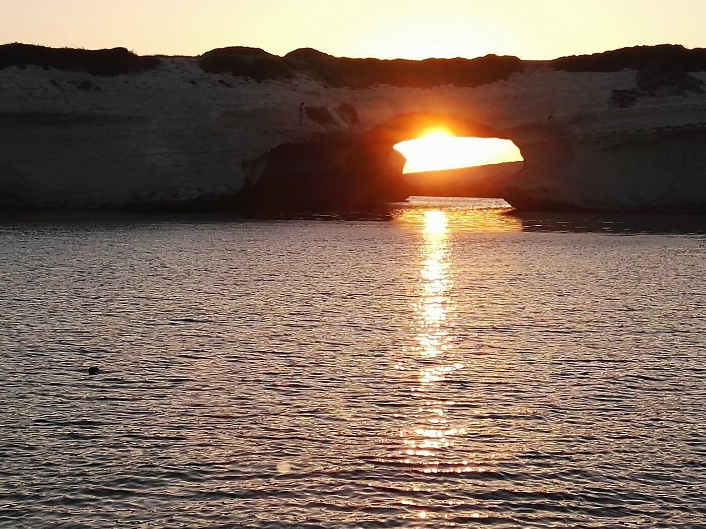 A sunset over a body of water with a rocky shoreline.