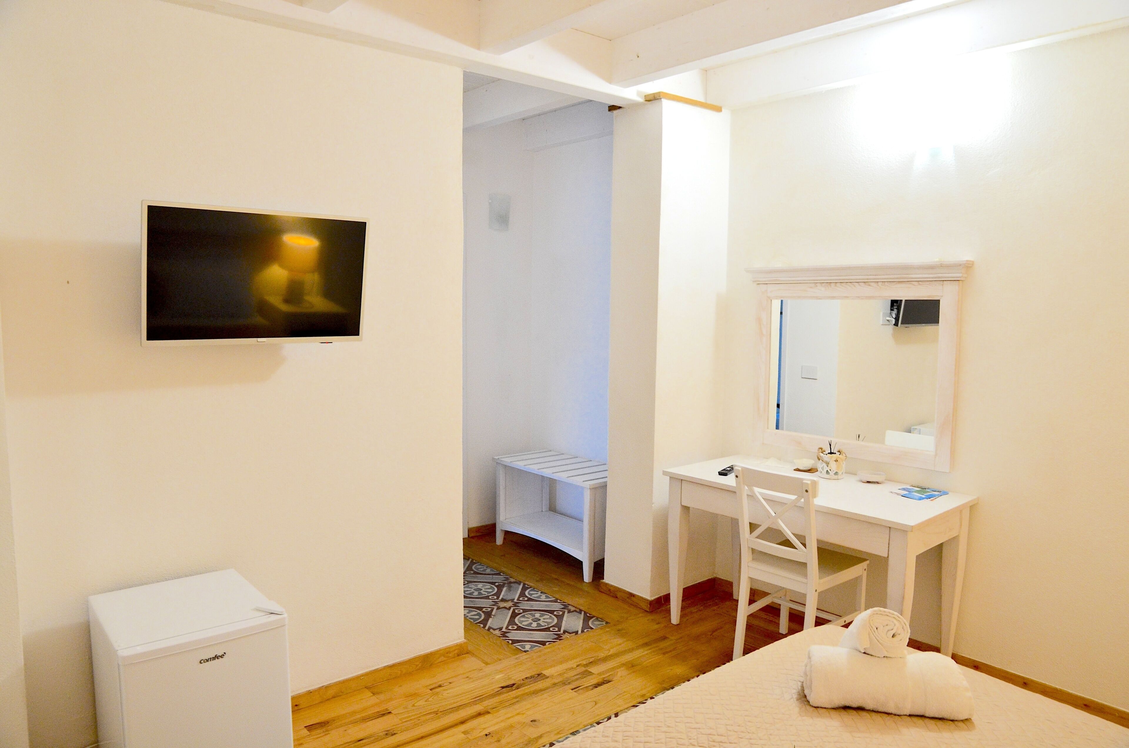 A bedroom with a bed, a desk, a chair, a television, and a small white cabinet.