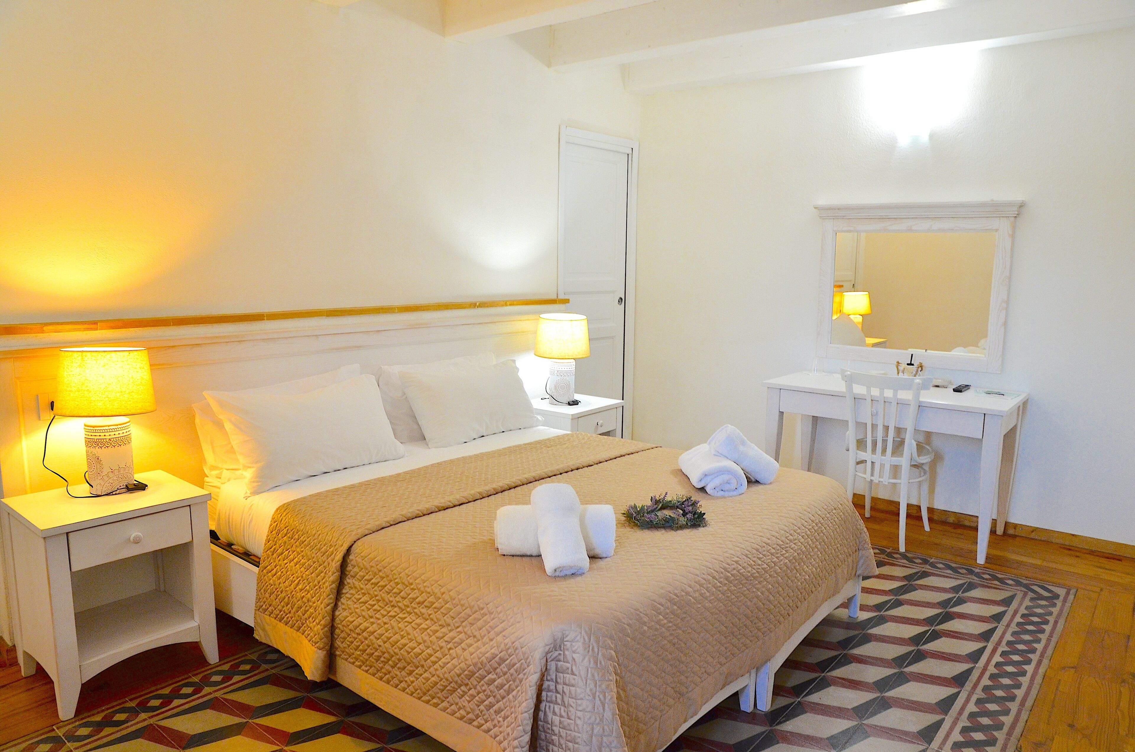 A hotel room with a bed, bedside lamps, a desk, a chair, and a mirror.