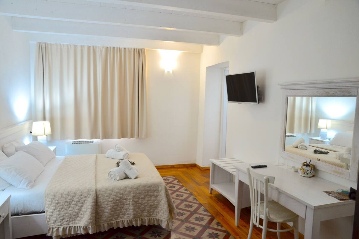 A hotel room with a bed, a desk, a chair, a TV, and a window with curtains.