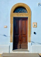 Puerta doble de madera con intrincados grabados, ubicada en un arco de piedra sobre un muro azul claro.