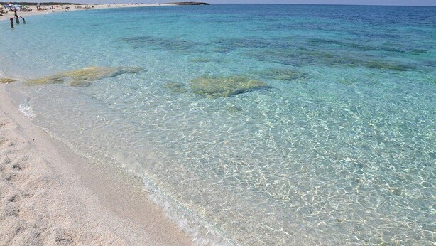 Una playa con aguas poco profundas y cristalinas y una orilla arenosa.