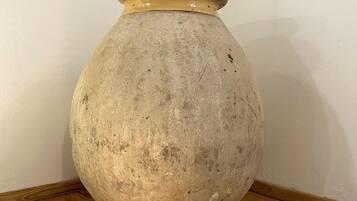 A large, round, beige ceramic vase with a narrow neck and a wider base, placed on a wooden table against a plain wall.