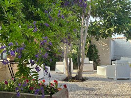 Un jardín con mobiliario exterior blanco, un árbol y plantas con flores.