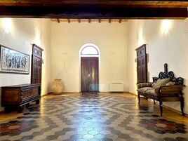 Un pasillo amplio con suelo de baldosas, un banco de madera, un sofá y una puerta con ventanal de arco.