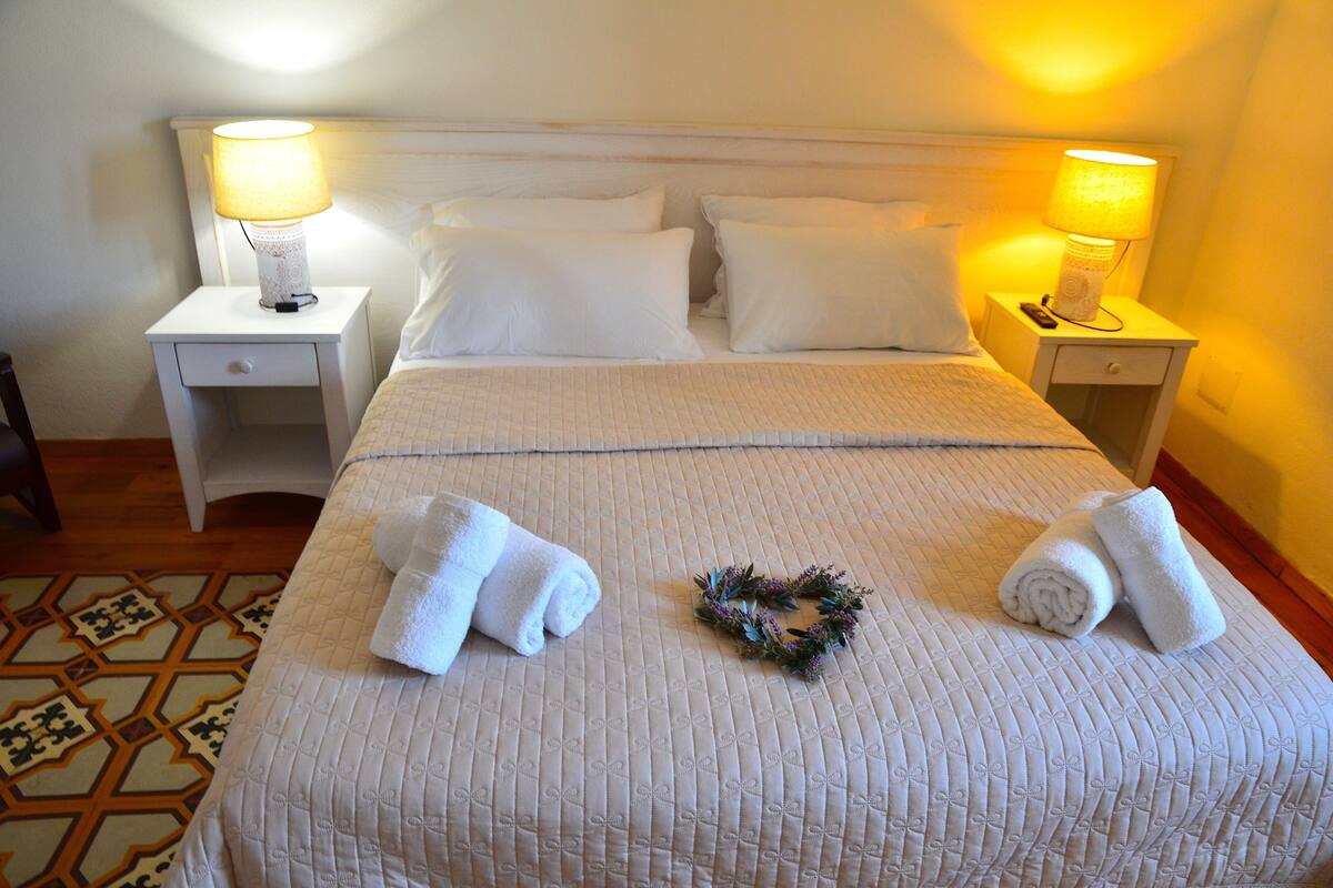 A neatly made bed with pillows, a bedside lamp, a folded towel, and a decorative wreath.