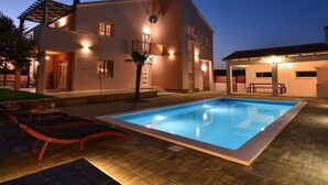 A modern house with a swimming pool, a covered patio, and a well-lit exterior at dusk. - Apartment Villa Troskot - Villa with pool (Pirovac)