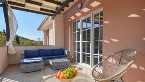 A balcony with a sofa, a wicker chair, and a table with a fruit bowl. - Apartment Villa Troskot - Villa with pool (Pirovac)
