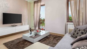A modern living room with a flat-screen TV, a glass coffee table, and a sofa with patterned cushions. - Modern Comfort with Shared Pool, Balconies & Lush Green Surroundings - One Bedroom Apartment (Kastav)