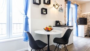 Una cocina moderna con una mesa redonda, sillas negras y un frutero. Hay tres cuadros con marco negro en la pared, una pared de piedra y un televisor sobre un mueble blanco.