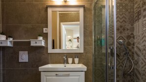Un baño con lavamanos blanco, espejo, inodoro y zona de ducha.