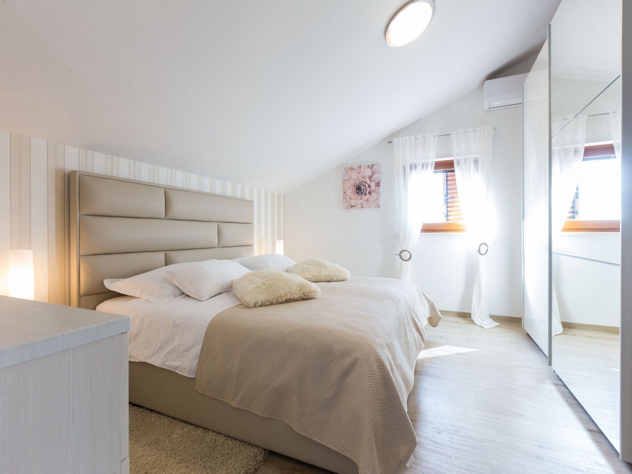 A bedroom with a bed, a bedside table, a mirror, and a window with curtains.