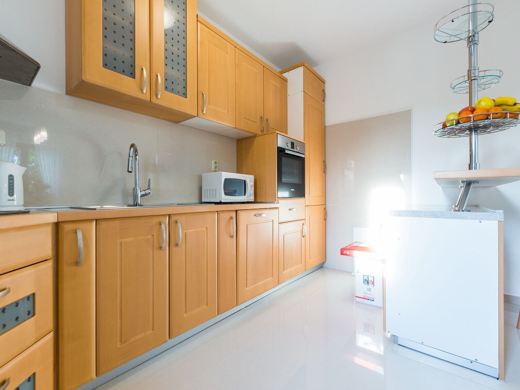 Una cocina moderna con armarios de madera, un refrigerador blanco, un microondas y una frutera sobre un pedestal.