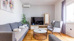 Una sala moderna con un sofá gris, una mesa de centro redonda, un televisor y una planta.
