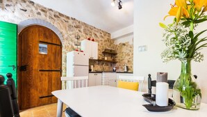 Een moderne keuken met een stenen muur, een houten deur, witte kasten en een eettafel met stoelen.