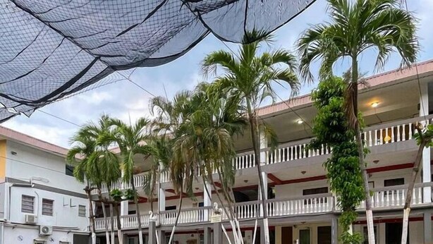 Un espace piscine avec une eau d’un bleu limpide, entouré de palmiers et bordé d’un immeuble à plusieurs étages doté de balcons.
