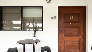 Une pièce avec une porte en bois portant le numéro 25, une table ronde avec deux tabourets noirs et une plante en pot posée sur la table.
