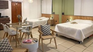 Une chambre d’hôtel avec deux lits simples, une table à manger avec des chaises, une petite table ronde avec un livre, et un coin cuisine.