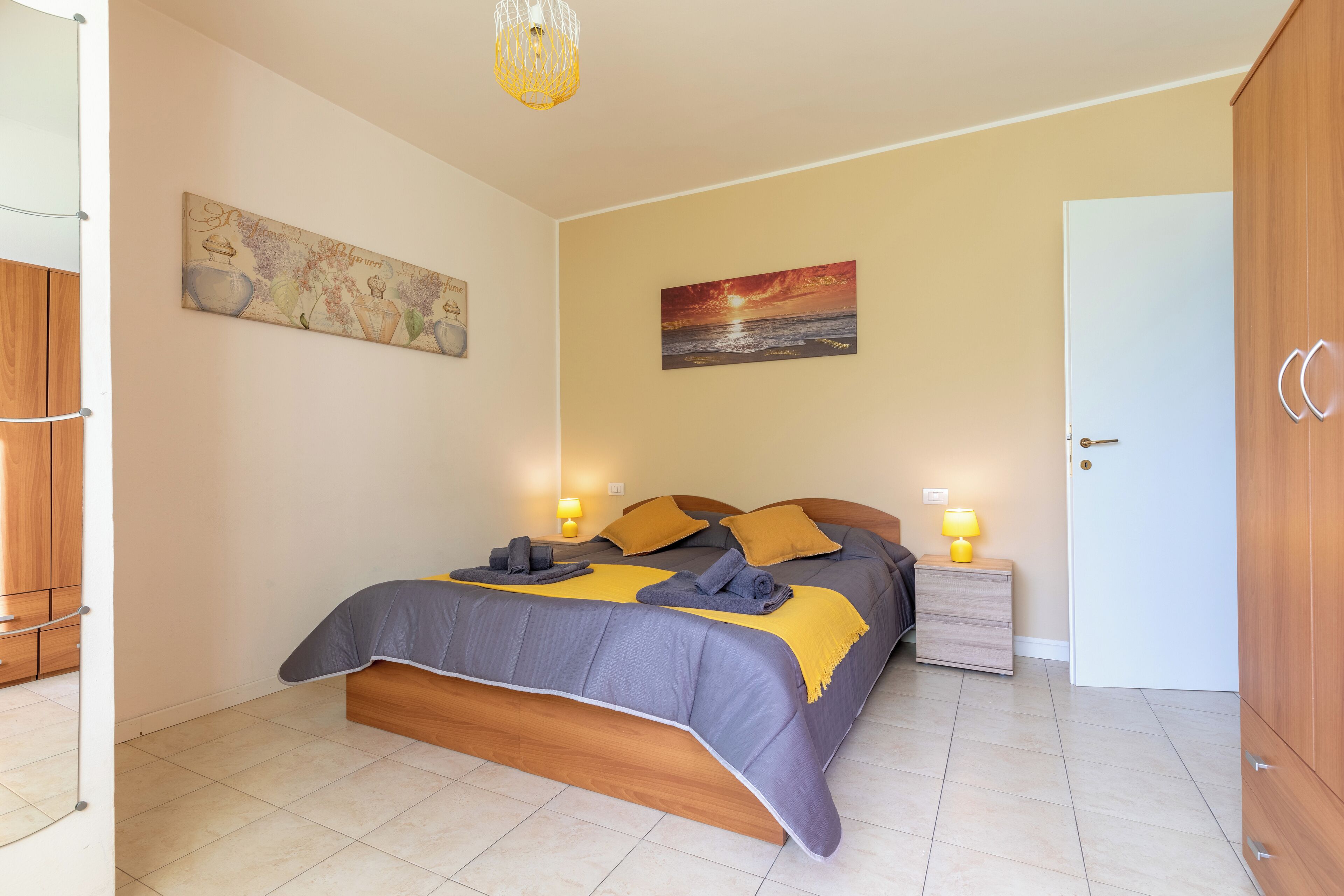 A bedroom with a bed, bedside lamps, a painting, and a wardrobe.