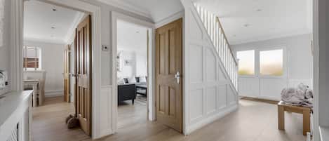 A spacious hallway with wooden flooring, a staircase, and a view into a living area with a sofa and a table.