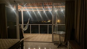 Un balcón con una hamaca, una mesita y vistas a una ciudad iluminada de noche.
