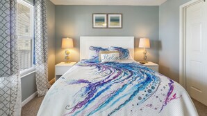 Ein Schlafzimmer mit einem Bett, zwei Nachttischlampen, einem Kopfteil mit einem 'Relax'-Kissen und zwei gerahmten Bildern an der Wand.