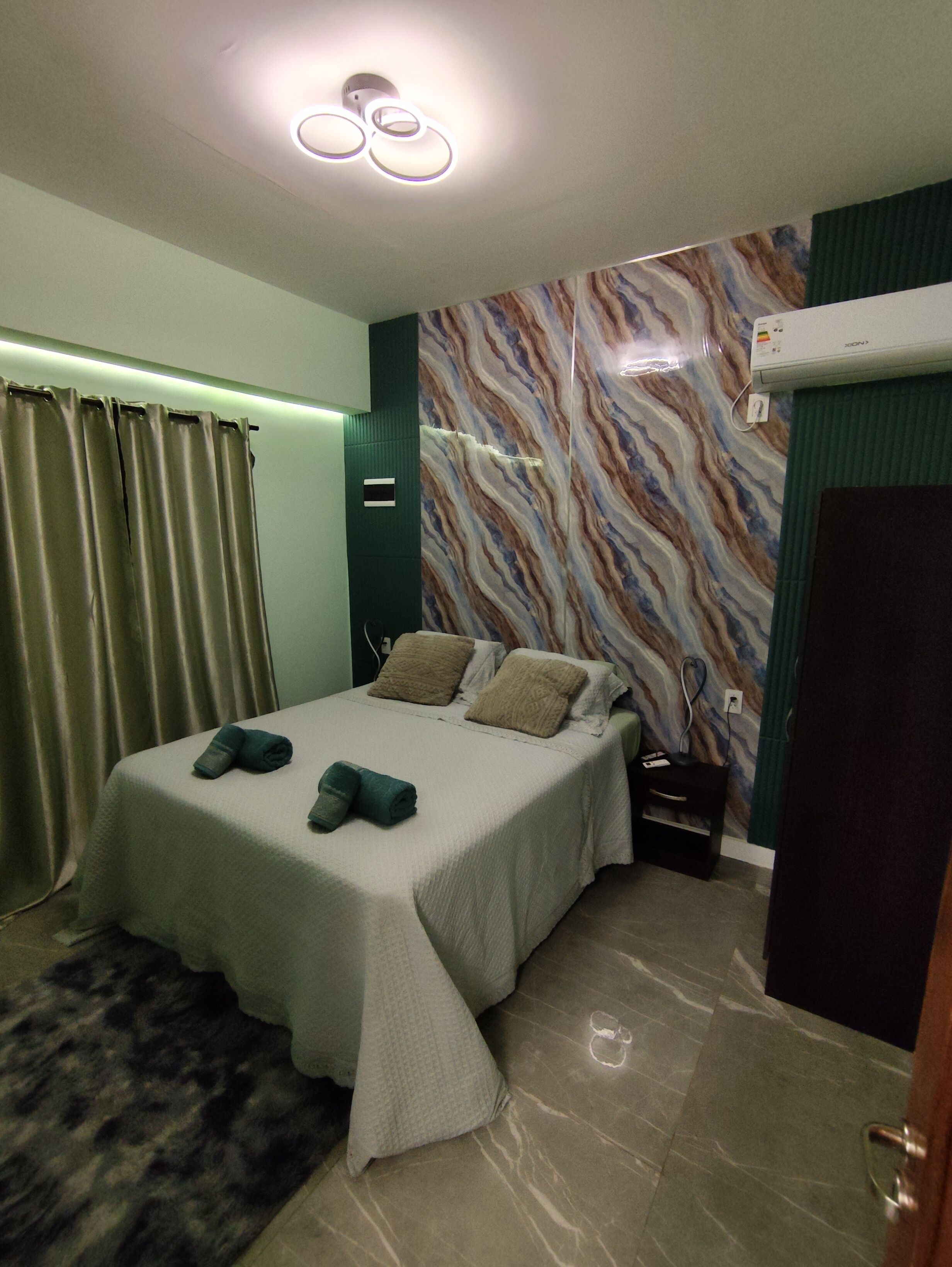 A modern bedroom with a bed, a nightstand, a wall-mounted air conditioner, and a patterned wall.