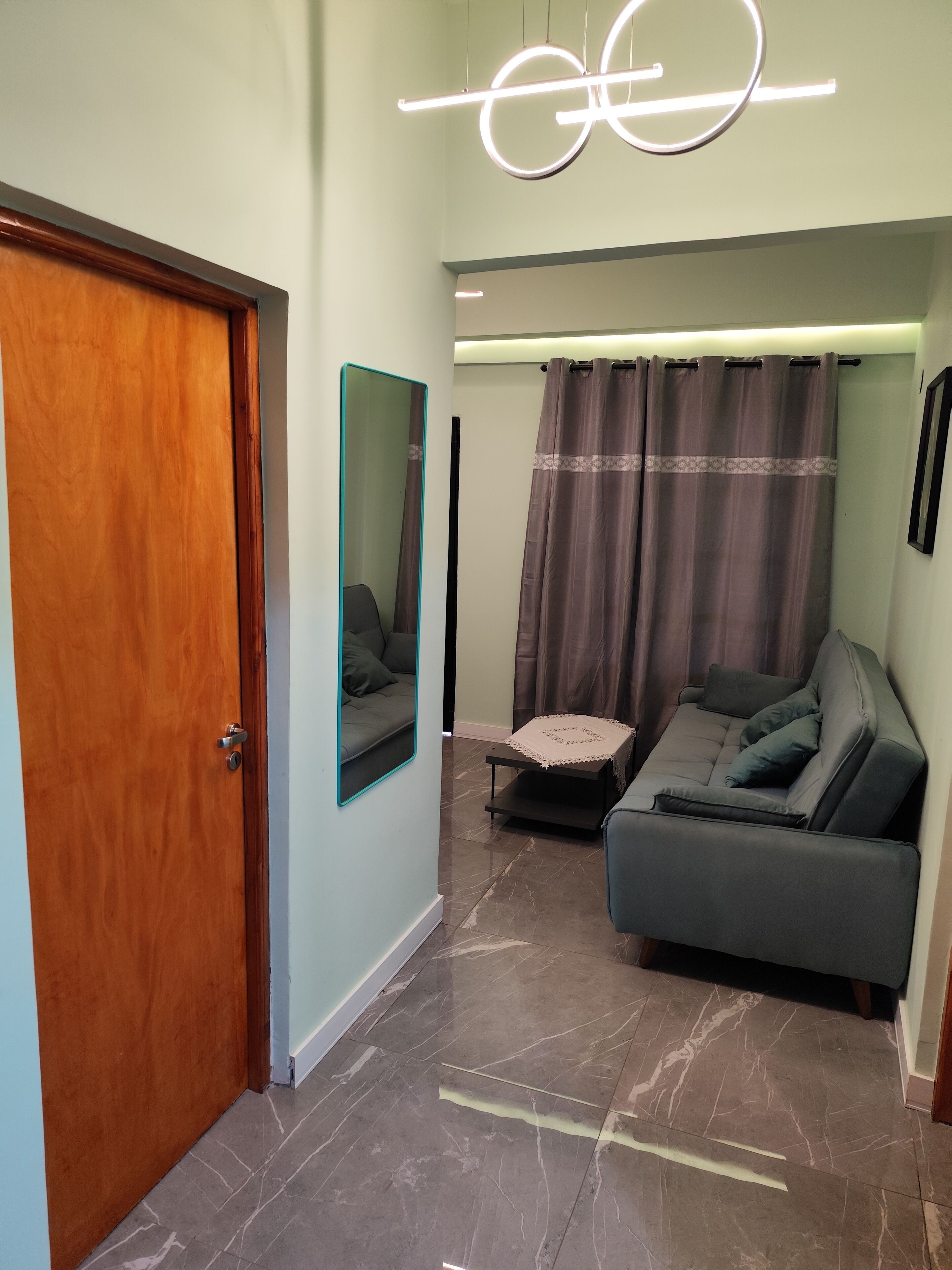 A modern living room with a wooden door, a sofa, a small table, and a mirror.