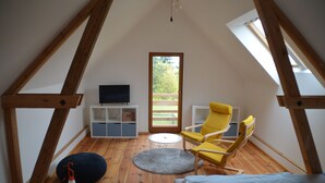 Une pièce avec un plafond en pente, une télévision, un fauteuil jaune, une table ronde et un lit.