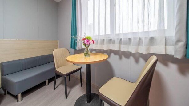 Una habitación con sofá, dos sillones, una mesita redonda con un florero y una ventana con cortinas.