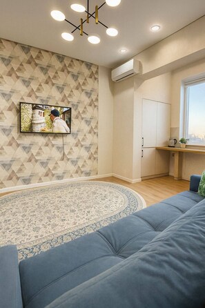 A modern living room with a patterned wall, a sofa, a coffee table, and a kitchen area with cabinets and a window.