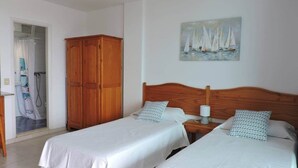 A bedroom with two beds, a wooden wardrobe, a painting of sailboats, and a shower area. - Mar de Lava (Puerto de Naos)