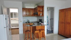 A compact kitchen with wooden cabinets, a central island with stools, and a visible shower area. - Mar de Lava (Puerto de Naos)