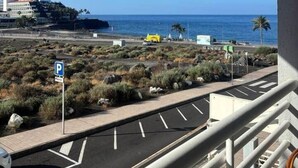 A balcony with a view of a parking area, a beach, and a building in the distance. - Mar de Lava (Puerto de Naos)