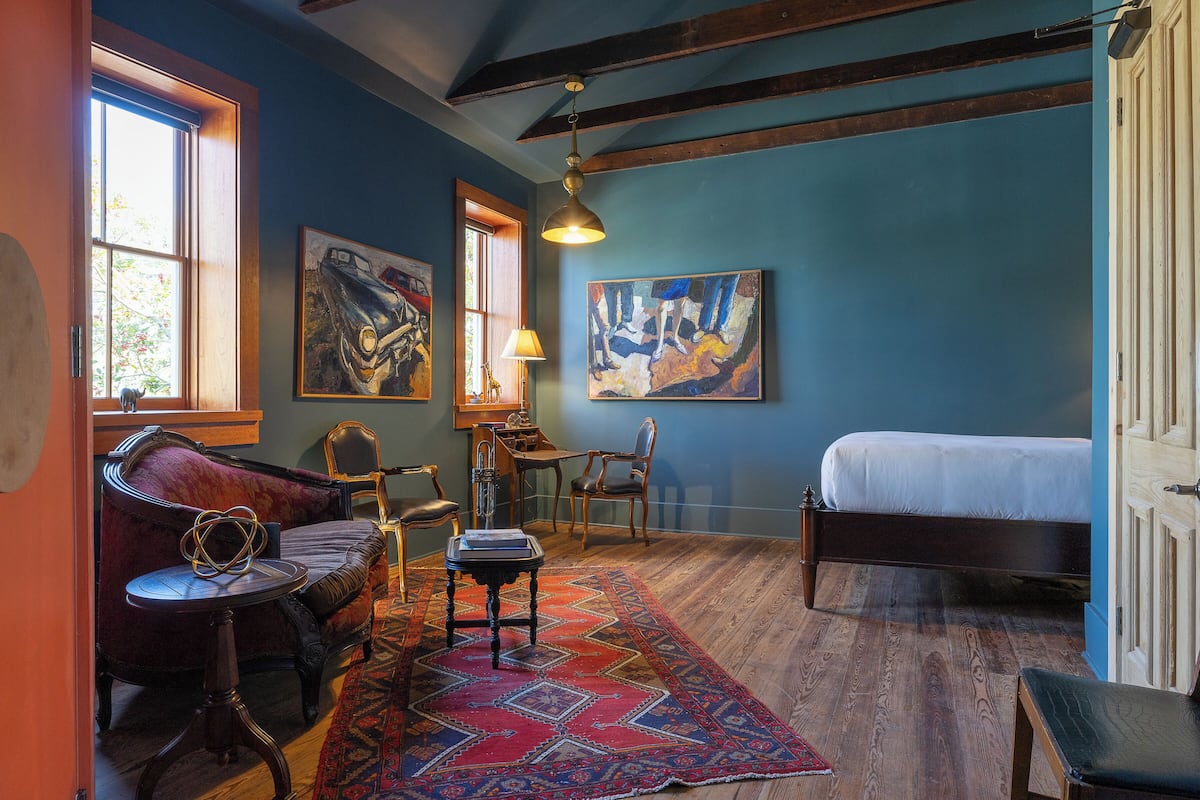 A room with a bed, a desk, a chair, a rug, and artwork on the walls.
