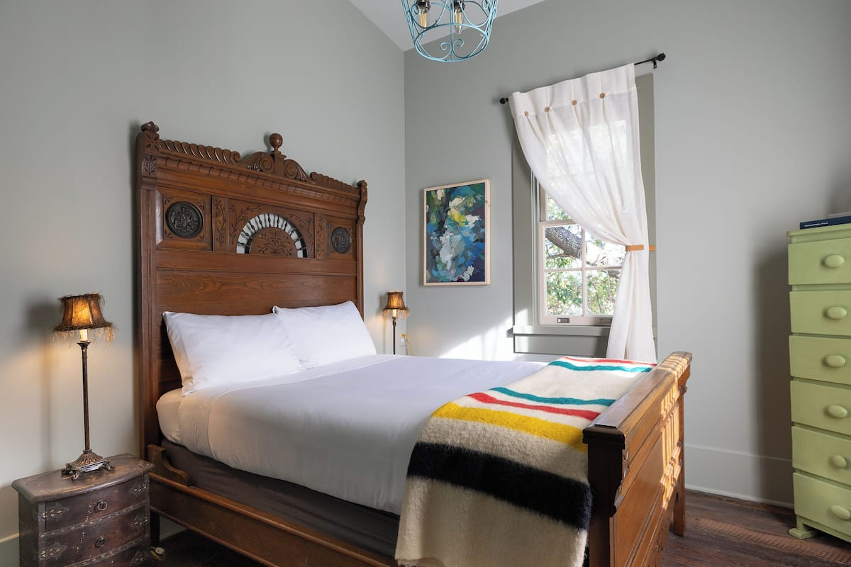 A neatly made bed with a wooden headboard, a bedside lamp, and a green dresser.