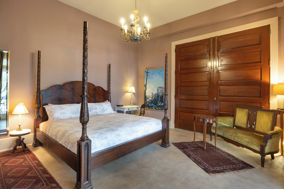 A spacious bedroom with a four-poster bed, a wooden wardrobe, a green sofa, and a chandelier.