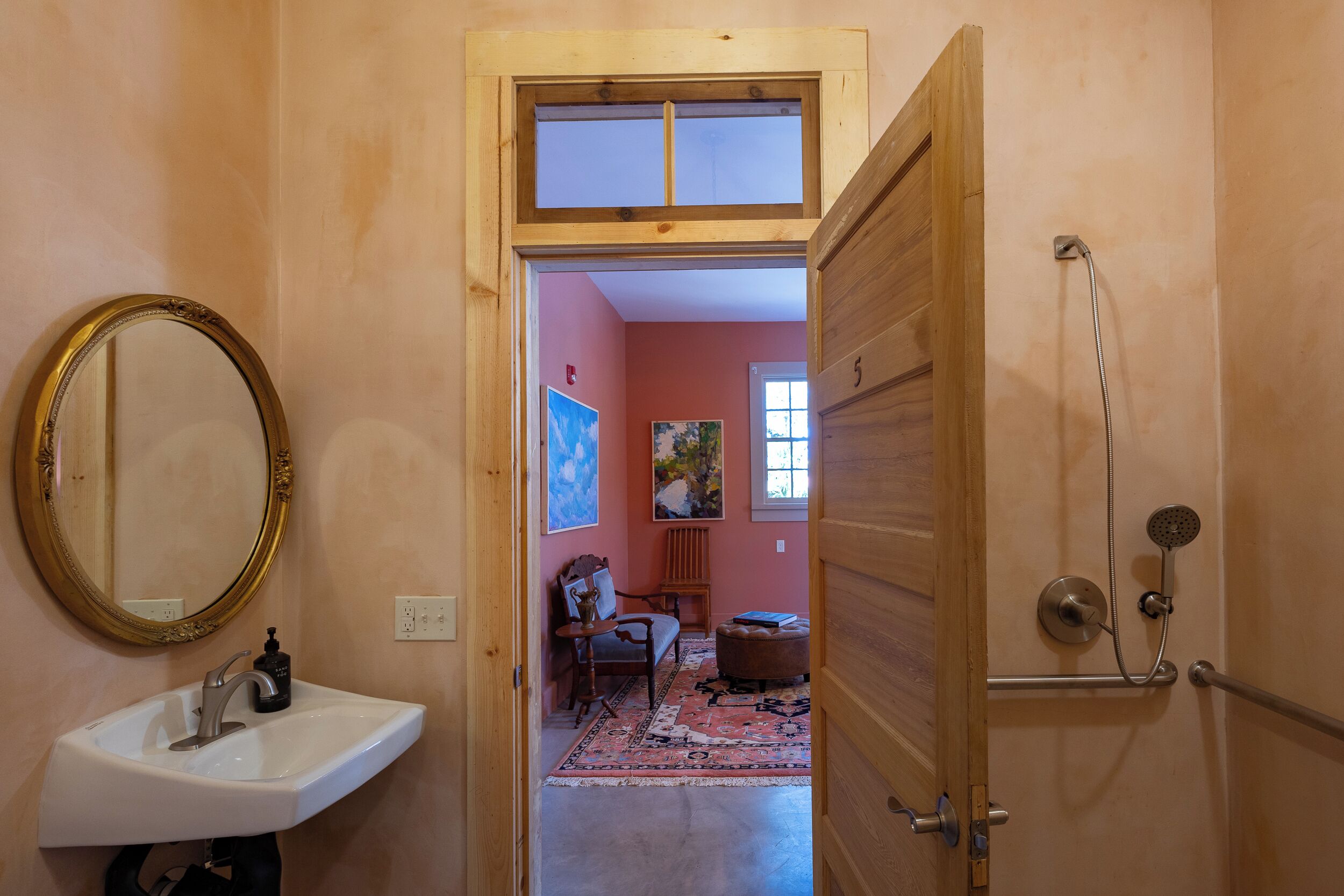 Un baño con lavamanos, espejo, ducha y una puerta que da a una sala de estar con alfombra y muebles.