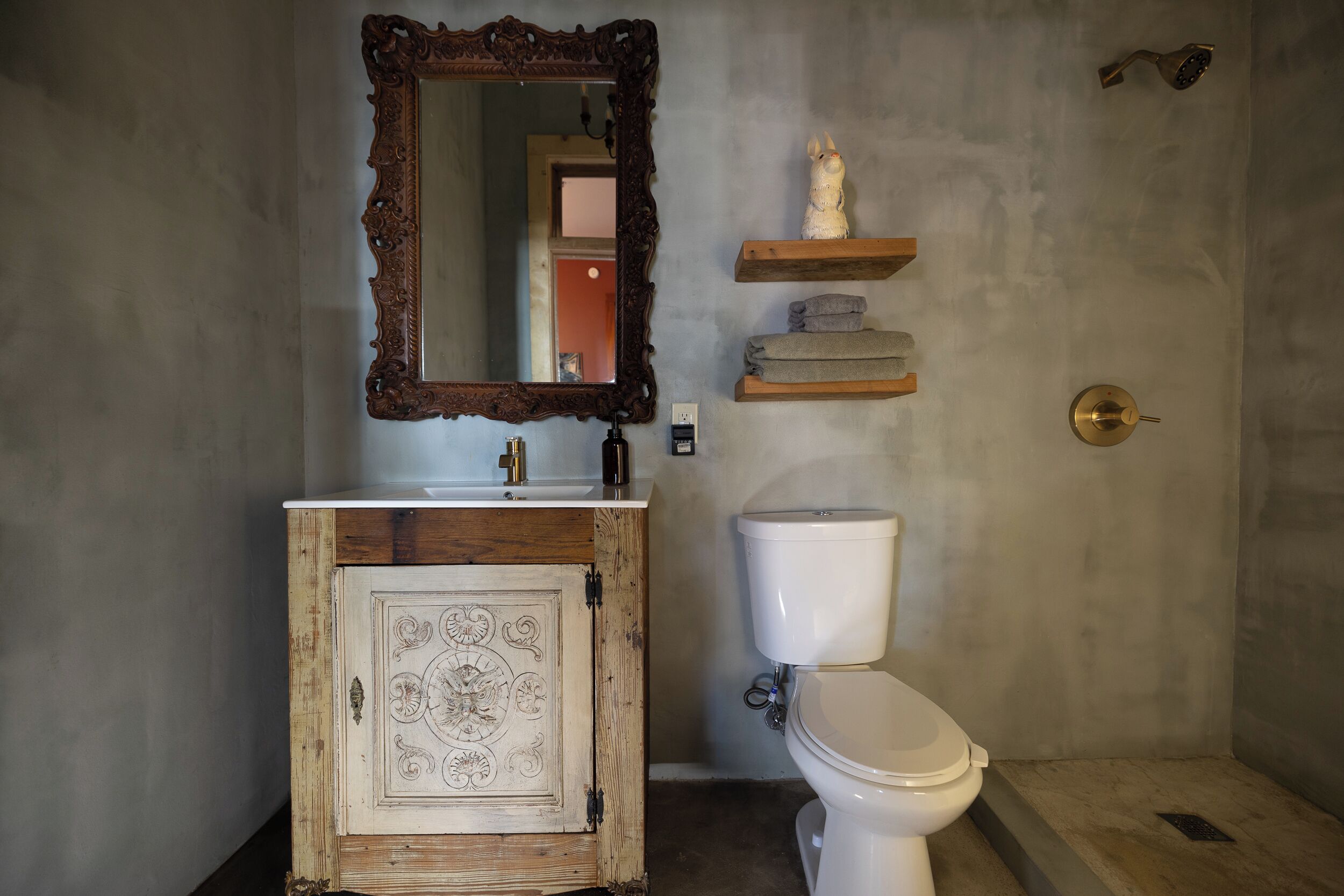 Un baño con un tocador rústico, un inodoro blanco, un espejo con marco decorativo y un perchero para toallas.