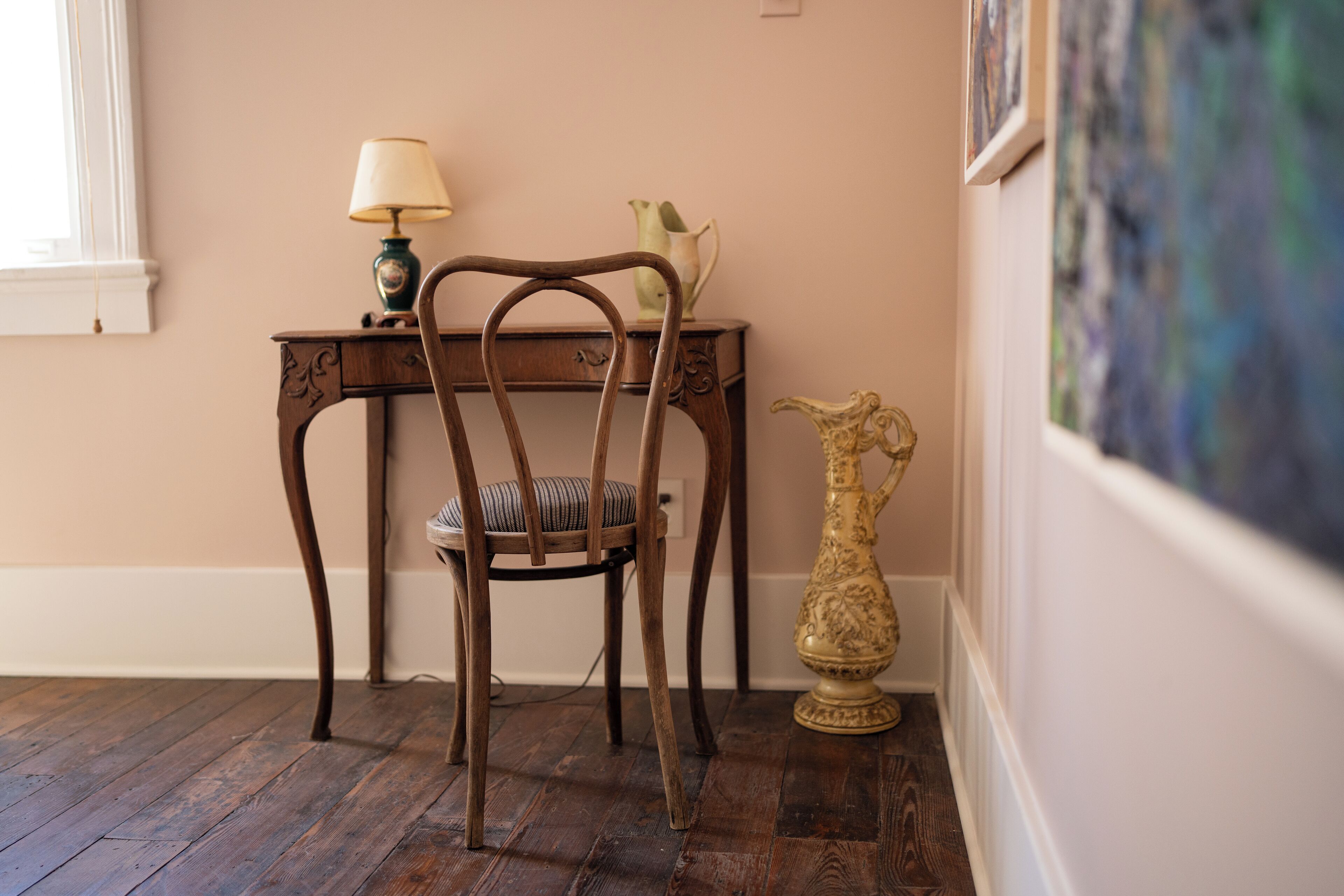 Una silla de madera con asiento acolchado, una mesita con lámpara y un jarrón decorativo en el suelo.