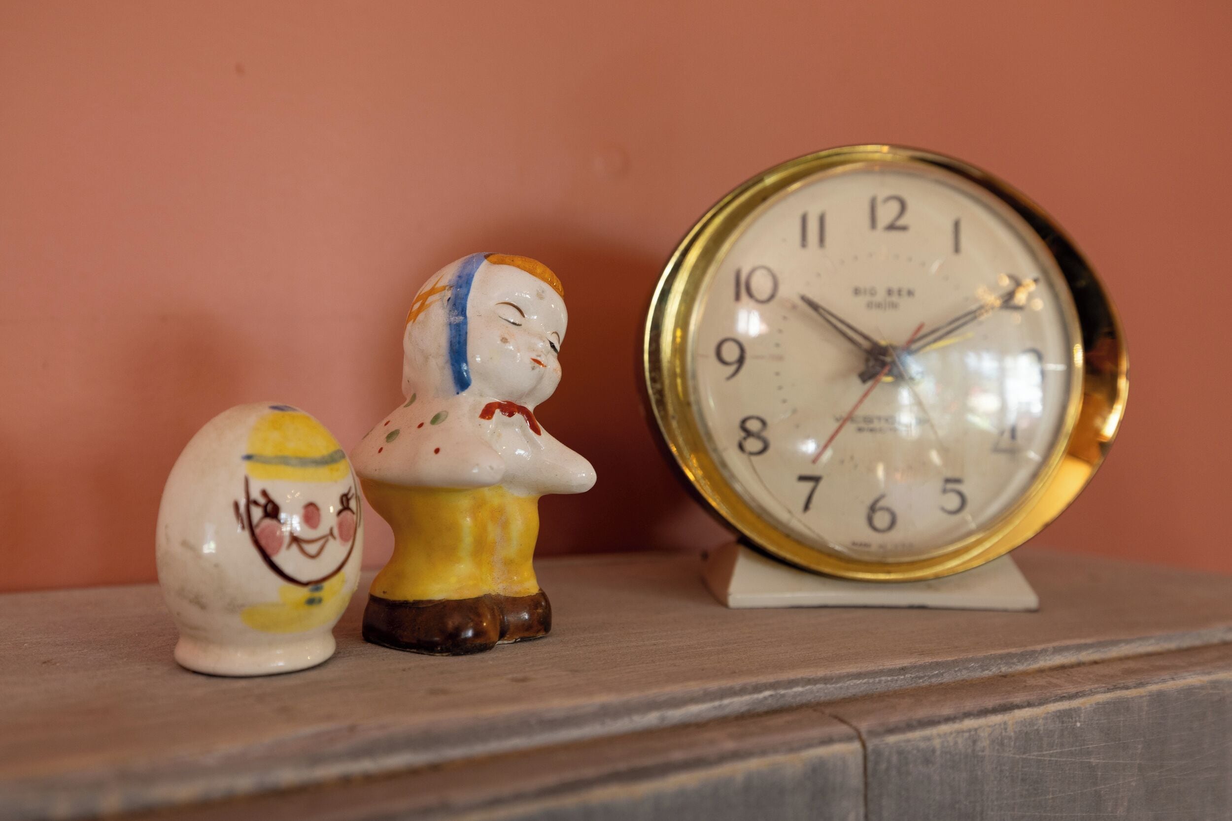 Una repisa con dos figuritas de cerámica y un reloj de pared.