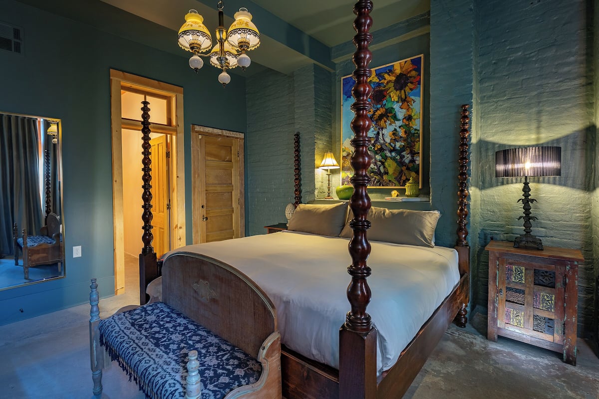 A bedroom with a four-poster bed, a bench, a painting, and a nightstand.