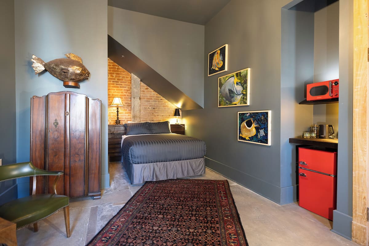 A bedroom with a bed, a wooden cabinet, a red cabinet, a red microwave, and a patterned rug.