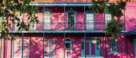 A two-story building with a pink facade, green trim, and a balcony.
